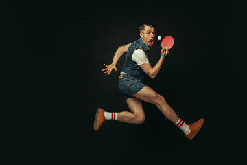 Young caucasian man playing tennis isolated on black studio background in retro style, action and...