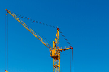 High yellow construction crane against the blue cloudless sky