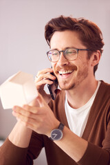Male Architect In Office Working At Desk Taking Call On Mobile Phone And Looking At Wooden Model