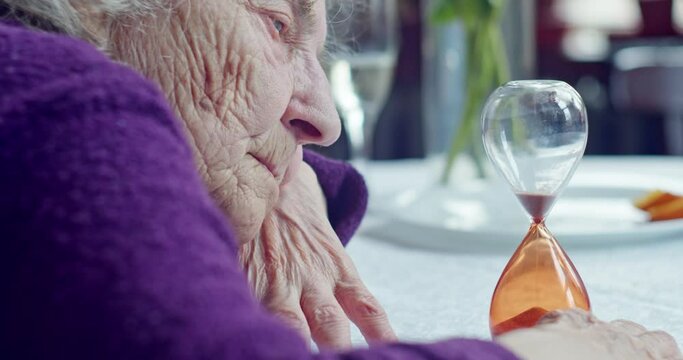portrait of an elderly woman looking at an hourglass in her home. an image of the value of providing timely assistance to old people. 