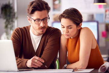 Male And Female Architects In Office Working At Desk On Laptop And Looking At Plans