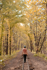Obraz premium A cinematic color graded backside portrait of a young Indian man walking on a railway track which is inside a dense green forest