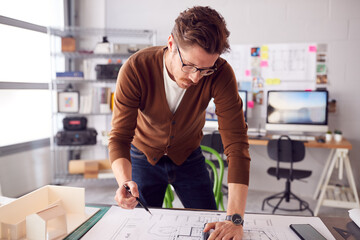 Male Architect Standing At Desk In Office Amending Building Plans