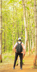 A 18-25 year old man wearing cap and standing in a forest with a bag. Full back side view of an Indian man.