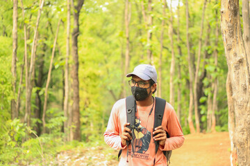 A 18-25 year old Indian man wearing a cap and a mask and walking freely in a jungle. Face towards the left side of the camera.