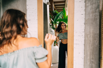 Ethnic woman in trendy clothes standing near mirror