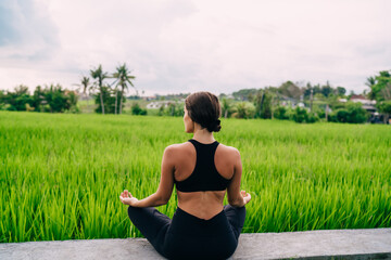 Back view of tranquil female looking at Indonesian landscape with rice fields and meditating for get mindfulness and enlightenment, slim woman in sportswear enjoying morning yoga practice in Thailand