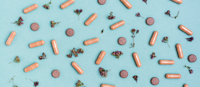Abstract green background with capsules, pills and herbs. Alternative medicine. Top view. Web banner