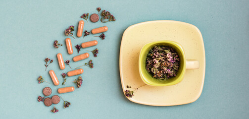 Medicinal capsules, pills and herbs in the form of a branch on a green background and a cup with oregano. Alternative medicine. Top view. Web banner