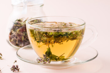 Fresh hot tea with oregano in a cup and dry herb in a jar. Herbal medicine and alternative therapy. Close-up