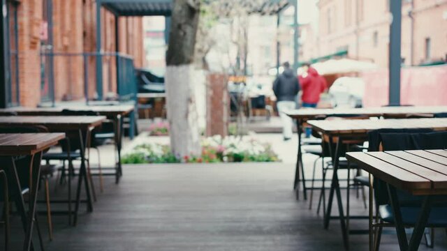 Cinematic real-time footage of wooden tables on the empty street veranda of the restaurant, people pass by.
