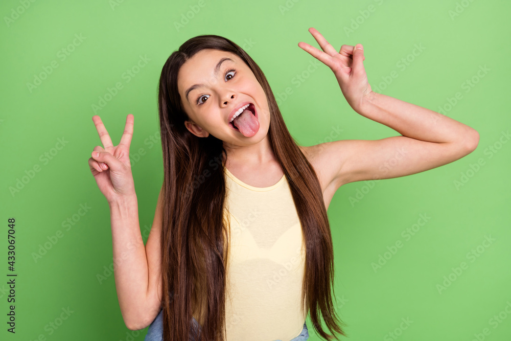 Wall mural Photo of cheerful excited girl tongue out fingers show v-sign have good mood isolate don green color background