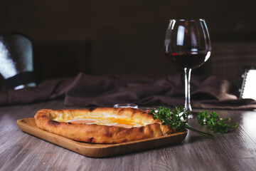 Khachapuri with egg, herbs and wine on the table in the cafe