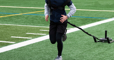Obraz premium Close up of athlete pulling a sled carrying extra weight on a turf field