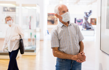 Obraz premium mature European man examines paintings in an exhibition in hall of an art museum
