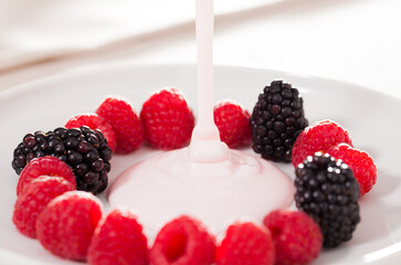 fresh raspberries and blackberries laid out on a white plate in circle with yogurt