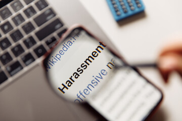 "harassment" word on phone's screen and magnifying glass close-up