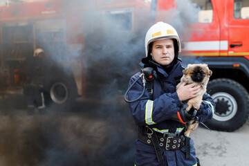 Firefighter in fire fighting operation. Portrait of heroic fireman in protective suit and white helmet holds saved dog in his arms