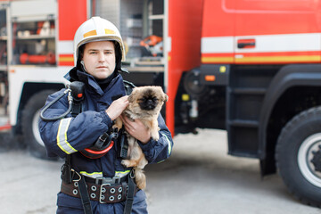 Firefighter in fire fighting operation. Portrait of heroic fireman in protective suit and white helmet holds saved dog in his arms