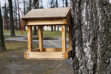 An old wooden bird feeder that hangs from a tree in the park.
