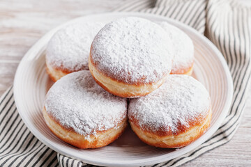 Delicious strawberry jam filled berliner doughnuts on white plate with napkin on wooden table top overhead