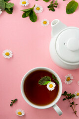 Cup and teapot of herbal tea with chamomile flowers and mint leaves on pink background