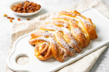 Sweet bun with cottage cheese and raisins on a serving board on a white kitchen table close-up. The concept of home-made high-calorie pastries	