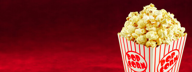 Full popcorn in a classic popcorn box on a red background.Popcorn spinning in circles around.	
 - obrazy, fototapety, plakaty