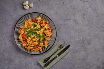 Scrambled eggs with cauliflower and tomatoes with herbs on a blue plate on a gray background