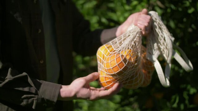 zero waste, plastic free recycled textile produce bag for carrying fruit. farmer holding fresh oranges in a net bag. Grocery shopping food supermarket. Delivery healthy food background.