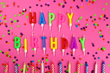 Colorful happy birthday candles and confetti on a pink pbackground