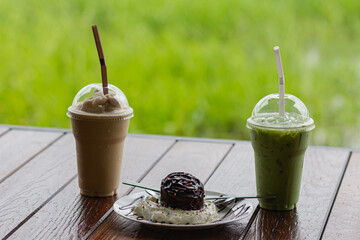 Two drinks and chocolate ice cream in a white plate. Behind is a meadow