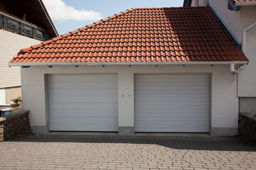 A modern and luxurious two-car garage with a tiled red roof and a roller door