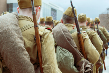 Soviet soldiers of the Second World War are marching. Infantry uniform khaki color, caps, rifles. Back view. - obrazy, fototapety, plakaty