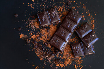 Broken chocolate bar pieces and cocoa powder on dark background
