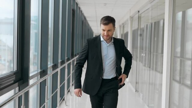 Business adult man walking down the hall receives a joyful message on a smartphone
