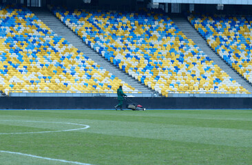 Worker mowing lawn on football field using grass-cutter