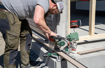tough construction worker cuts wooden siding with a tilt saw while building a garage