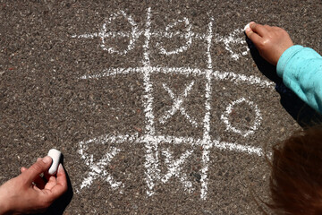 child plays with his mother in tic-tac-toe chalk on the asphalt