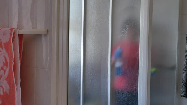 woman sanitizing shower box windows with blue bactericidal spray against viruses