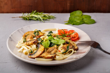 Udon with mushrooms and spinach in a plate on a concrete background next to a fork.