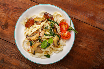 Udon with mushrooms and spinach and cherry tomatoes in a plate on a wooden table.