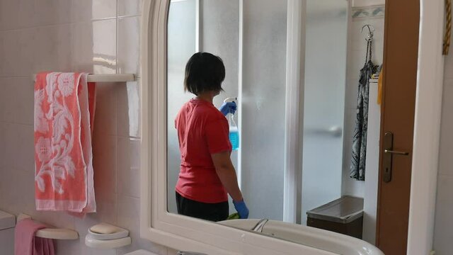 woman sanitizing shower box windows with blue bactericidal spray against viruses