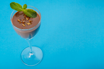 Chocolate cocktail with nuts and mint in a glass on a blue background.