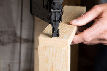 the hands of a carpenter using a power nailer to assemble two pieces of wood