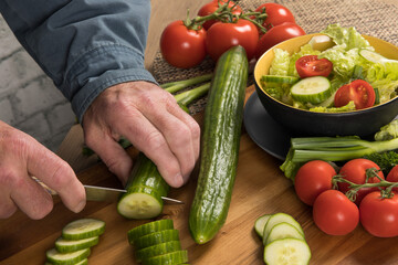 Hands cutting Red Tomatoes and green English cucumber slices and quarters in a salad

