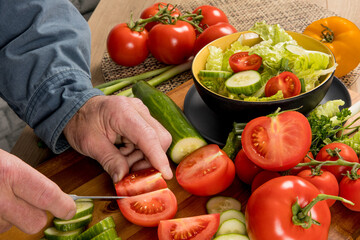 A cook's hands cutting Red Tomatoes and green English cucumber slices and quarters in a salad
