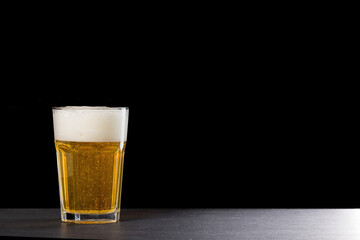 A full glass of light beer with a foam head isolated on a black background