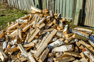 A pile of birch wood on the ground near the house.