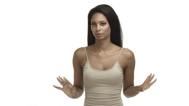 Serious african-american female model in beige tank top, shaking hands and saying no, decline bad idea, prohibit and reject something, standing over white background